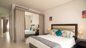 A hotel room with a large bed, a wardrobe, a mirror, and a nightstand with a lamp. - Apartments 125 (Gaborone)