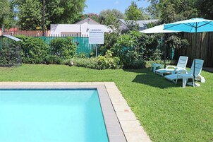 Una piscina con un cartel, césped y sillas de descanso.