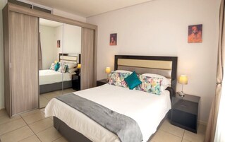 Una habitación de hotel con una cama grande, un armario, una mesita de noche y un espejo.