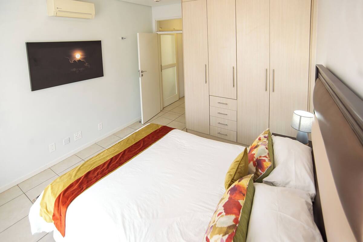 A hotel room with a bed, a wardrobe, a nightstand, a lamp, and a wall-mounted TV.