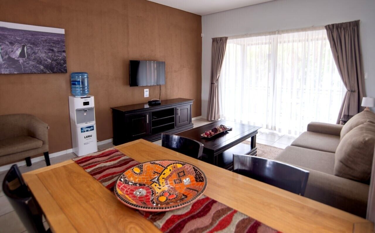 Een woonkamer met een bank, een eettafel met een decoratief bord, een waterdispenser, een televisie en een raam met gordijnen.