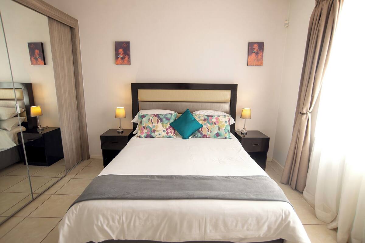 A hotel room with a bed, two bedside tables with lamps, a mirror, and artwork on the walls.