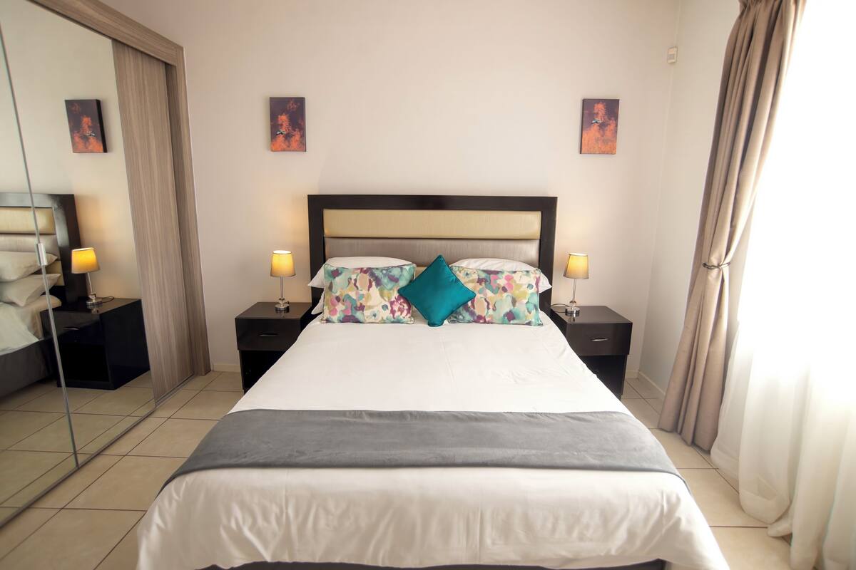 A hotel room with a bed, two bedside tables, a mirror, and artwork on the walls.