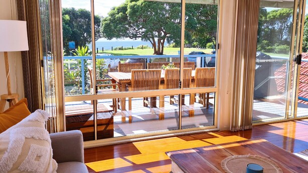 A room with a large sliding glass door leading to an outdoor patio with wooden furniture and a view of the sea. - Sea Whispers - ocean outlook, walk to 3x beaches (Port Macquarie)
