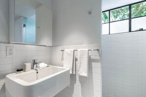 A modern bathroom with a large white bathtub, a mirror, and a window with a view of trees. - Blueground Oaxaca CDMX (Mexico City)
