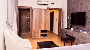 A modern hotel room with a wooden wardrobe, a desk with a chair, a flat-screen TV, and an air conditioning unit. - Jukky Hotel (Abuja)