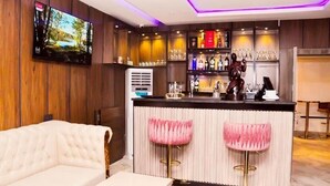 A bar area with a TV, bar stools, and a counter with bottles and glasses. - Jukky Hotel (Abuja)
