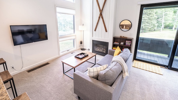 A modern living room with a flat-screen TV, a fireplace, and a large window overlooking a deck. - Tranquil 2-bedroom condo in Park City-Clubhouse pool/hot tub, free bus to resort (Park City)