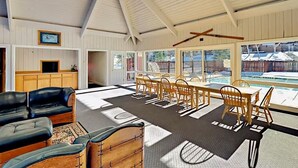 A spacious indoor area with a dining table and chairs, a black leather sofa, and a view of a swimming pool outside. - Tranquil 2-bedroom condo in Park City-Clubhouse pool/hot tub, free bus to resort (Park City)