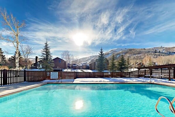 A clear blue pool surrounded by a wooden fence, with a mountain backdrop and a wooden cabin.