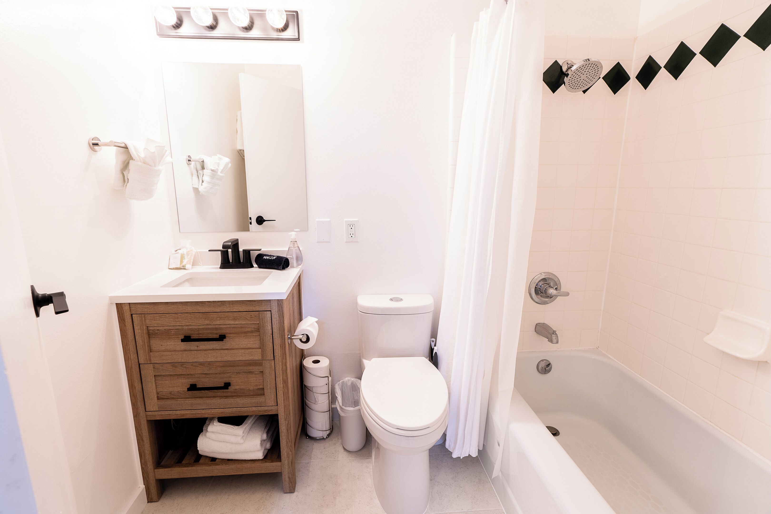 Un baño con tocador de madera, lavamanos blanco, espejo, inodoro y bañera.