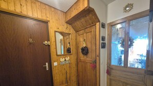 A wooden interior with a stone-tiled floor, a wooden door, a mirror, and a window with frosted glass. - Appartement familial au Revard, vue sur le jardin d'enfant et pistes (Les Deserts)