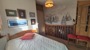 A bedroom with a bed, a wooden headboard, a window, and a wall with framed pictures. - Appartement familial au Revard, vue sur le jardin d'enfant et pistes (Les Deserts)