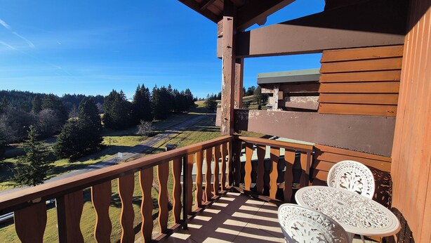 A balcony with a wooden railing, two white ornate chairs, and a view of a forested landscape. - Appartement familial au Revard, vue sur le jardin d'enfant et pistes (Les Deserts)