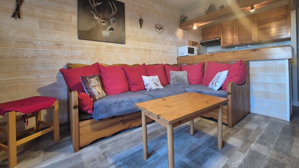 A cozy living area with a wooden sofa, red cushions, a wooden coffee table, and a kitchen area with wooden cabinets and a microwave.