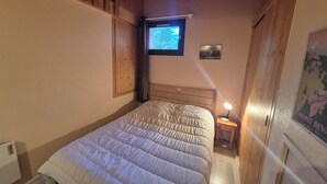 A bedroom with a bed, a nightstand with a lamp, a window, and a poster on the wall.