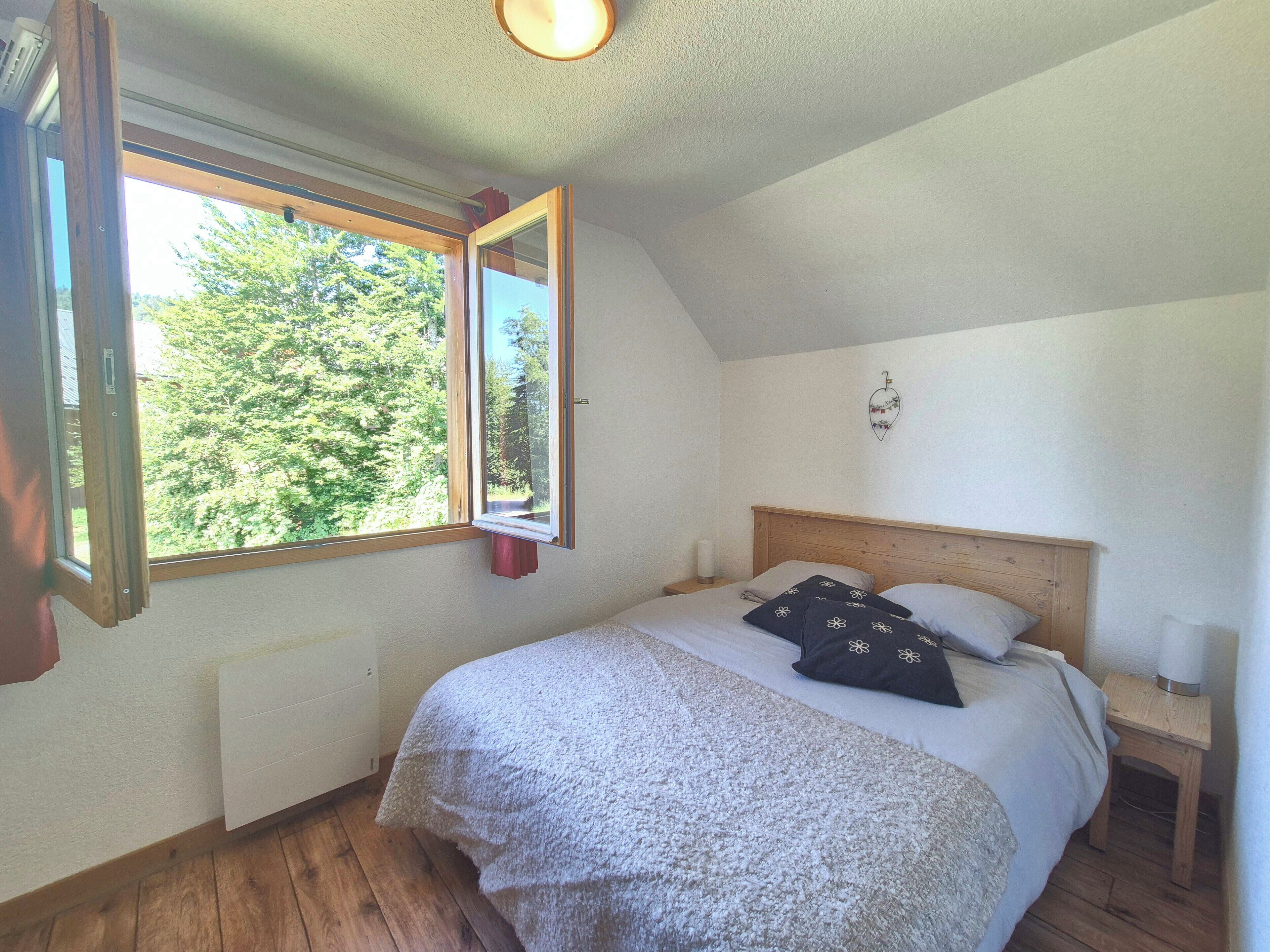Une chambre à coucher avec un lit en bois, une table de chevet, une fenêtre donnant sur des arbres et un luminaire au plafond.