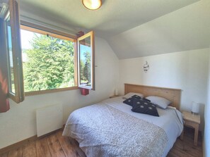 Et soveværelse med en træseng, et natbord, et vindue med udsigt til træer og en loftslampe.