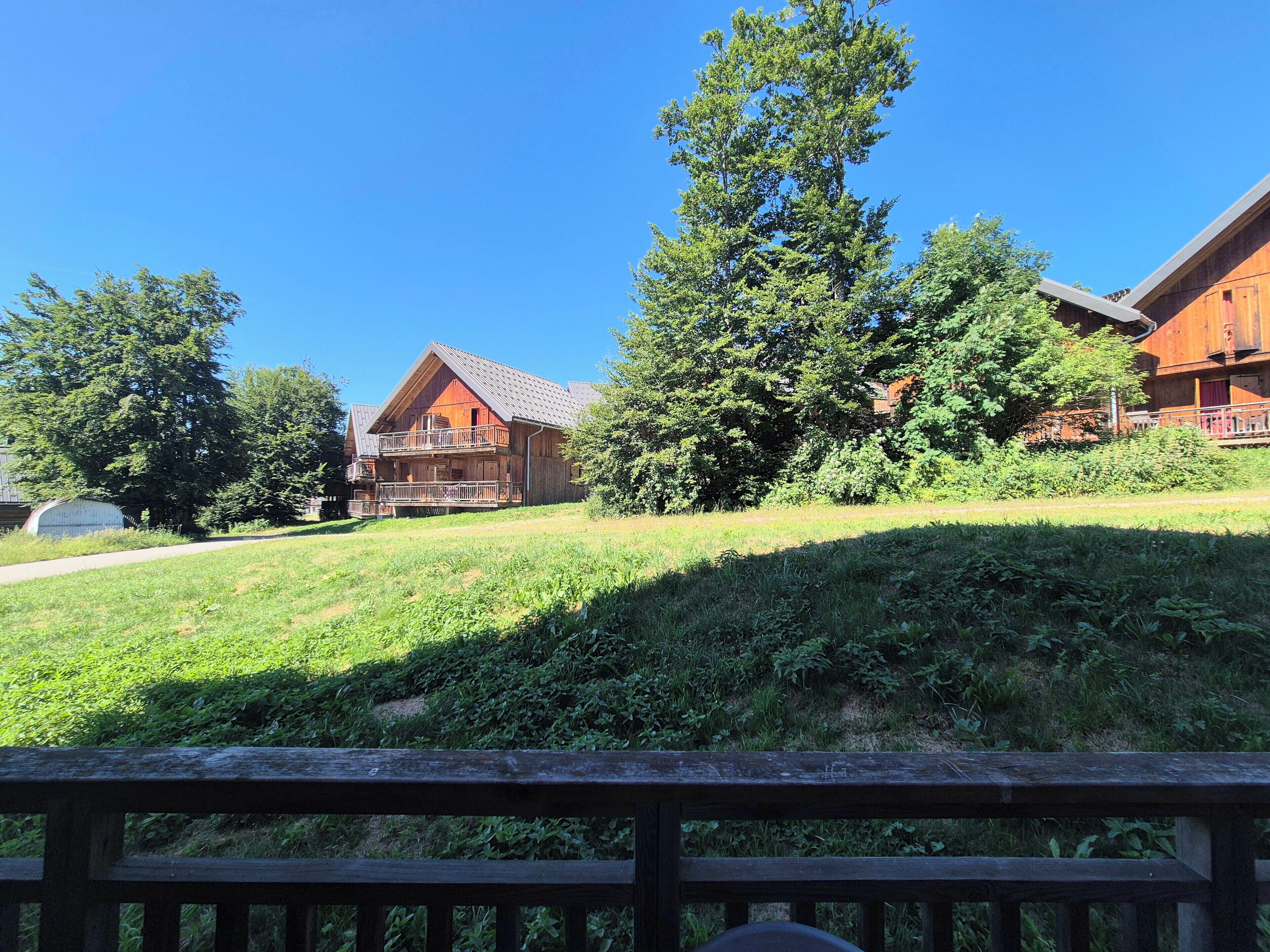 Eine Holzhütte mit Balkon, umgeben von viel Grün und Bäumen.