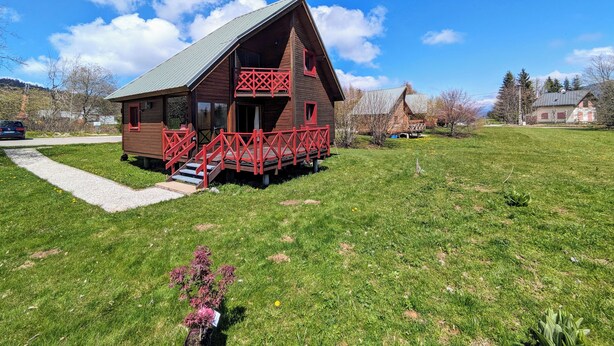A wooden cabin with a red balcony, surrounded by a grassy field and trees. - Chalet nordique, 6 personnes (La feclaz)