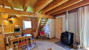 A cozy cabin interior with a dining area, a sofa, a fireplace, and a staircase leading to an upper level. - Chalet nordique, 6 personnes (La feclaz)