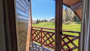 A wooden balcony with a red lattice railing, overlooking a green landscape with trees and a clear sky. - Chalet nordique, 6 personnes (La feclaz)
