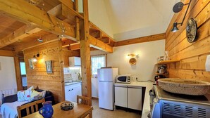 A compact kitchen with wooden walls, a dining area with a table and chairs, and a refrigerator. - Chalet nordique, 6 personnes (La feclaz)