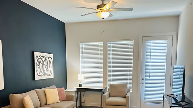 A modern living room with a dark blue accent wall, a beige sofa, a round coffee table, and a ceiling fan. - Cozy apartment in pleasant Leander with WiFi, AC (Leander)