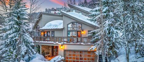 A two-story house with a garage, surrounded by snow-covered trees.