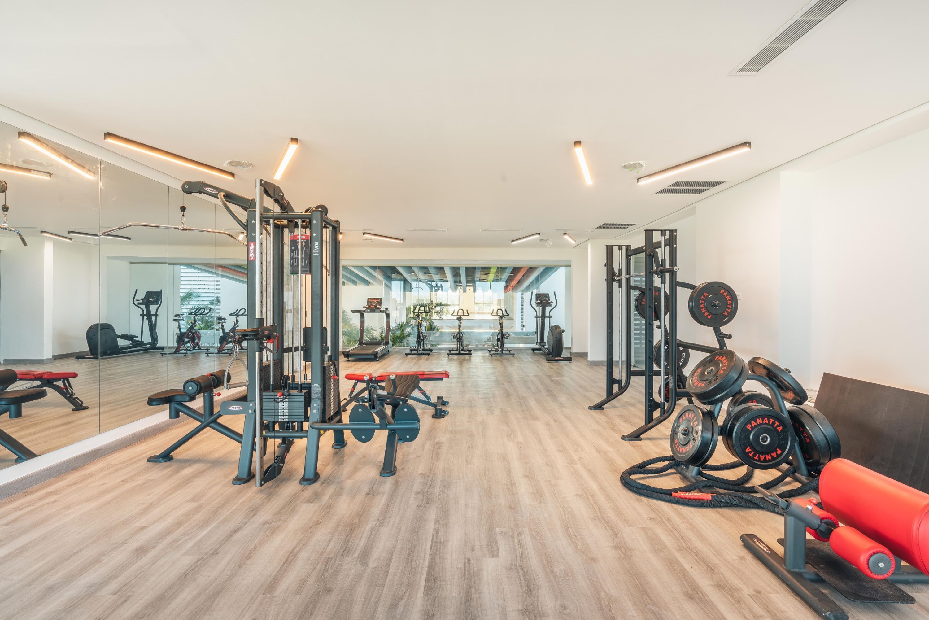 Ein Fitnessstudio mit unterschiedlichen Trainingsgeräten, Spiegeln und Holzboden.