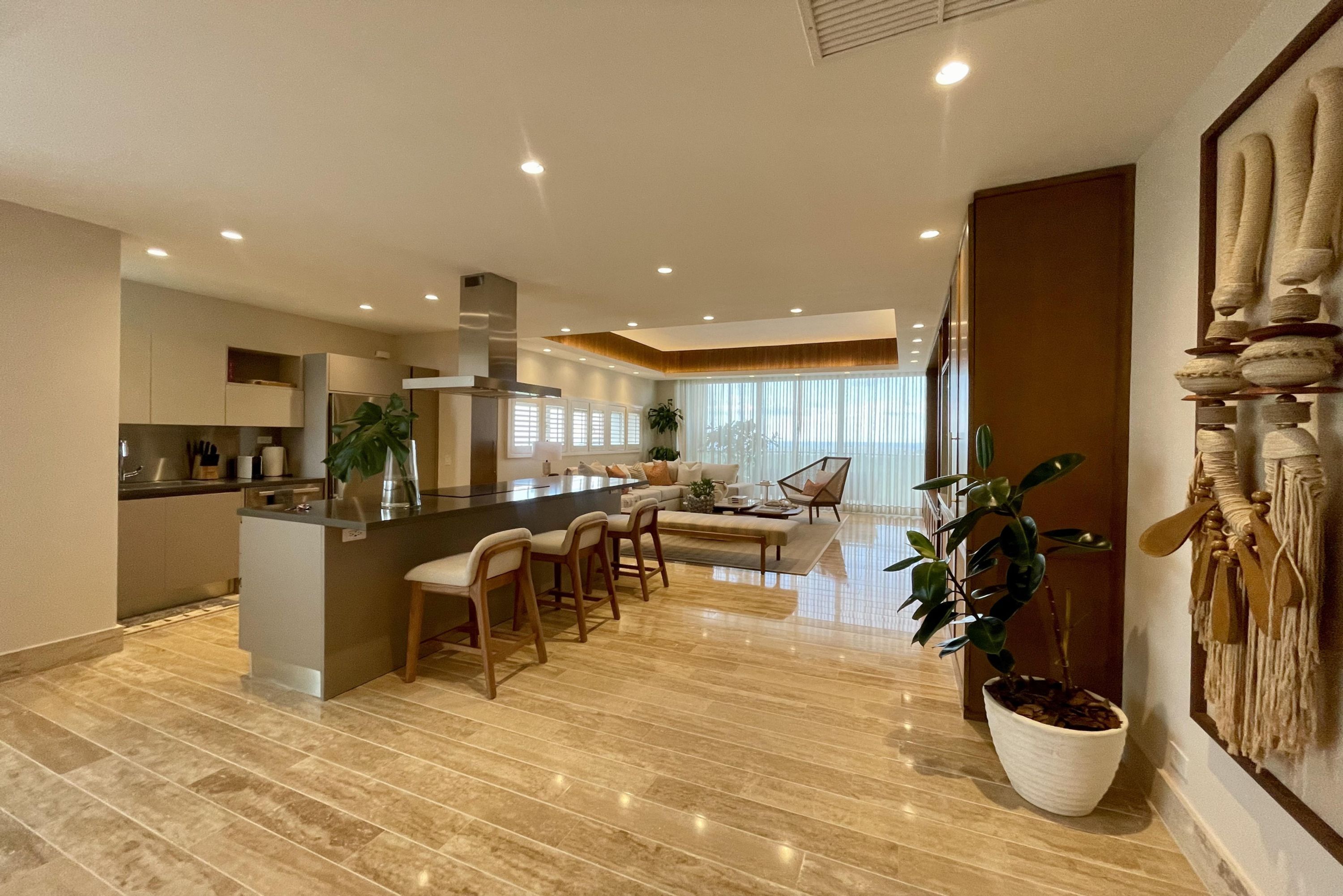 A modern kitchen with a central island, a dining area with chairs, and a large potted plant.