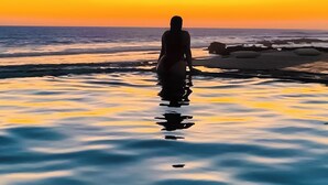 A silhouette of a person standing in shallow water at sunset. - Nochtli Beach House (Playas Negras)
