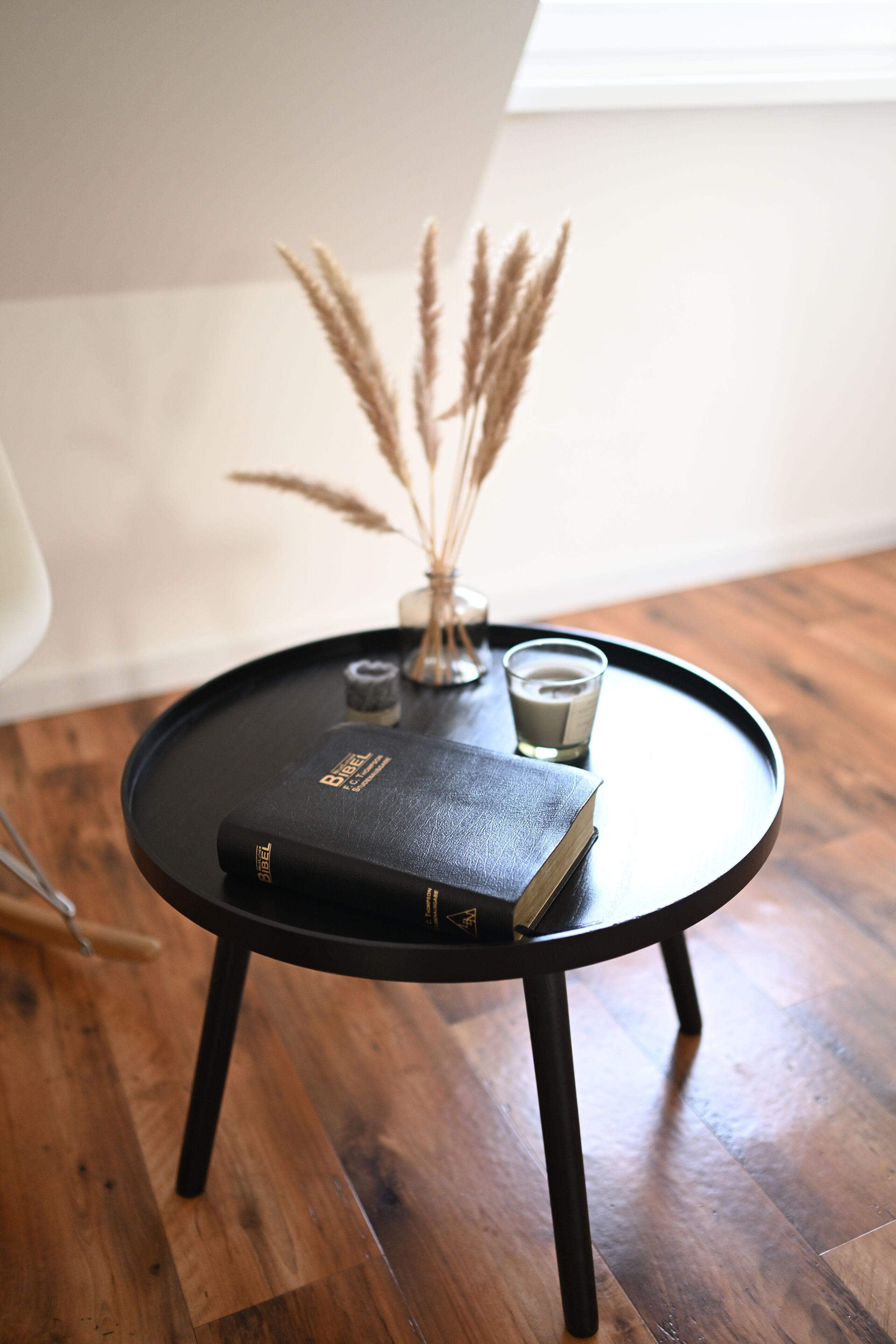 A small round table with a book, a candle, and dried plants.
