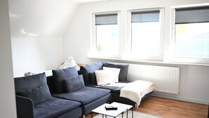 Una sala de estar moderna con un sofá seccional gris oscuro, una mesa de centro blanca y una ventana con persianas.