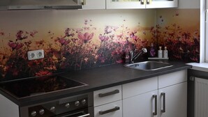 Una cocina moderna con armarios blancos, una campana de acero inoxidable, encimera negra y salpicadero con motivos florales.