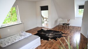 Una habitación moderna con un ventanal grande, un sofá blanco, un tapiz de cuero y una pequeña mesa con velas.