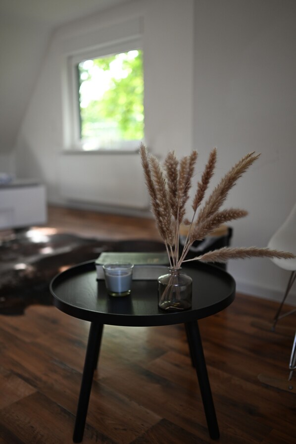 Una mesa redonda negra con un florero de vidrio que contiene plantas secas, un pequeño recipiente de vidrio y una vela.