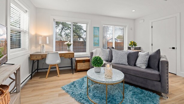 A modern living room with a grey sofa, a round coffee table, a wooden desk, and a TV on the left. - Chic Garden Suite (Victoria)