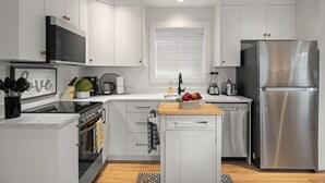 A modern kitchen with white cabinets, stainless steel appliances, and a central island. - Chic Garden Suite (Victoria)