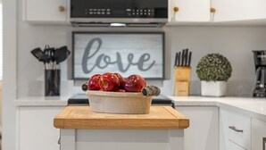 A kitchen counter with a bowl of apples and a decorative item, a framed word "love" on the wall, and kitchen utensils in the background. - Chic Garden Suite (Victoria)