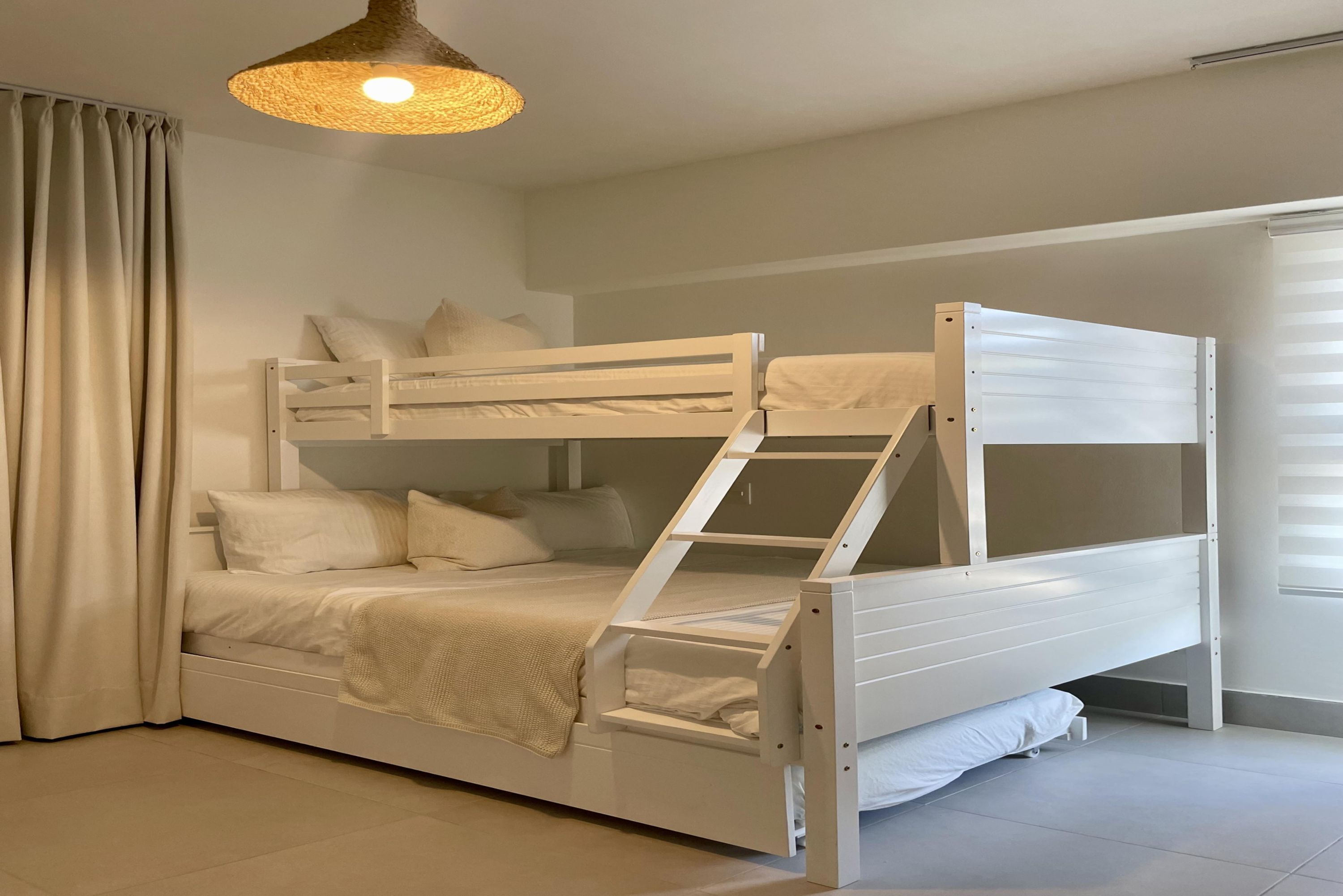 Un lit superposé avec une échelle, du linge de lit blanc et un luminaire suspendu.