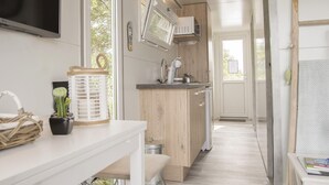 A modern kitchen with wooden cabinets, a sink, and a window. There is a white countertop with a basket and a plant.