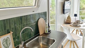 A modern kitchen with a stainless steel sink, green tiled backsplash, and a dining area with white chairs and a table.
