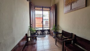 A hallway with a wooden bench, a potted plant, and a door with a metal gate. - Casona Macondo (Granada)