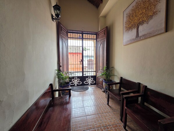 A hallway with a wooden bench, a potted plant, and a door with a metal gate.