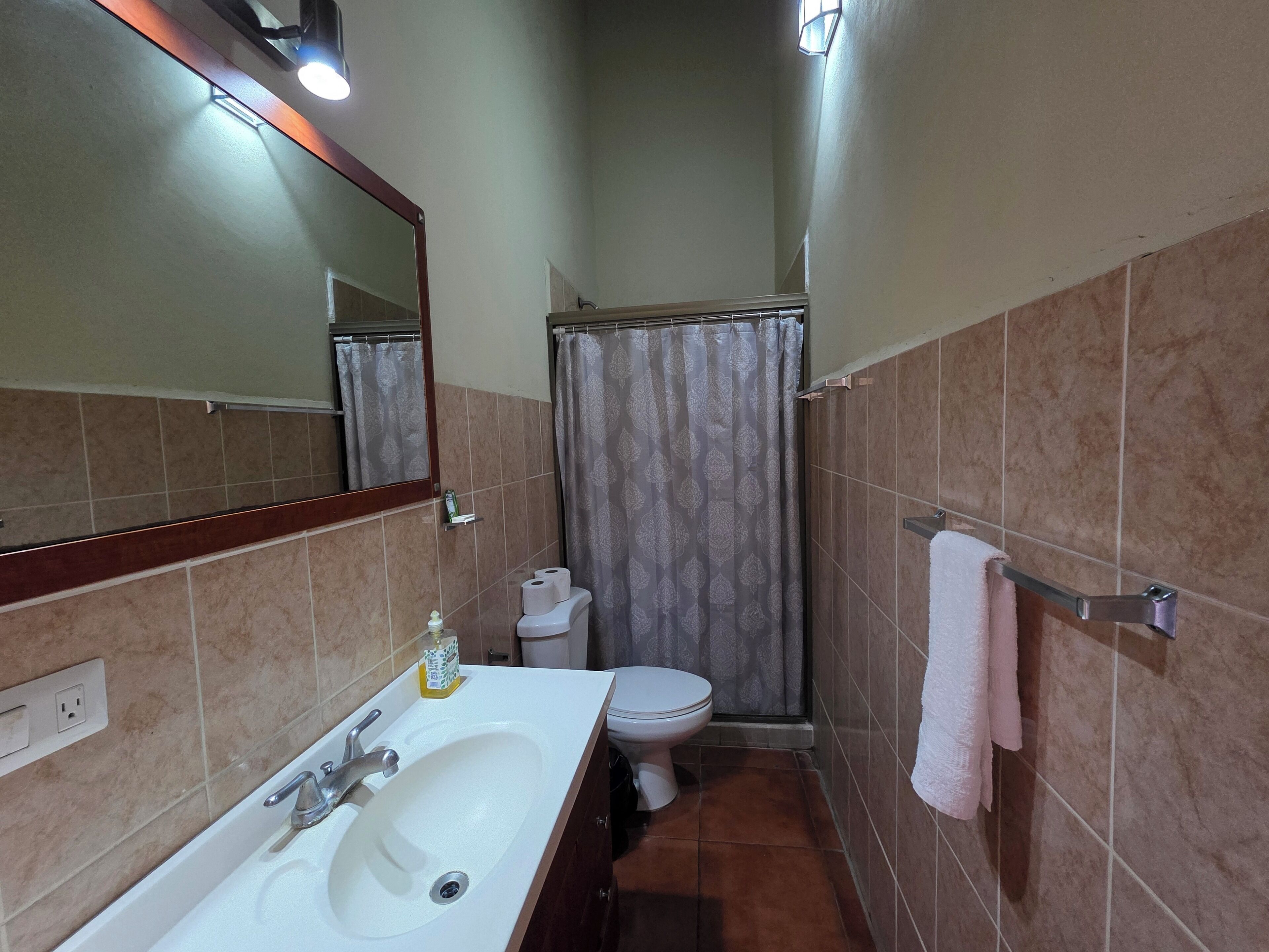 Un baño pequeño con lavamanos, espejo, inodoro y cortina de ducha.