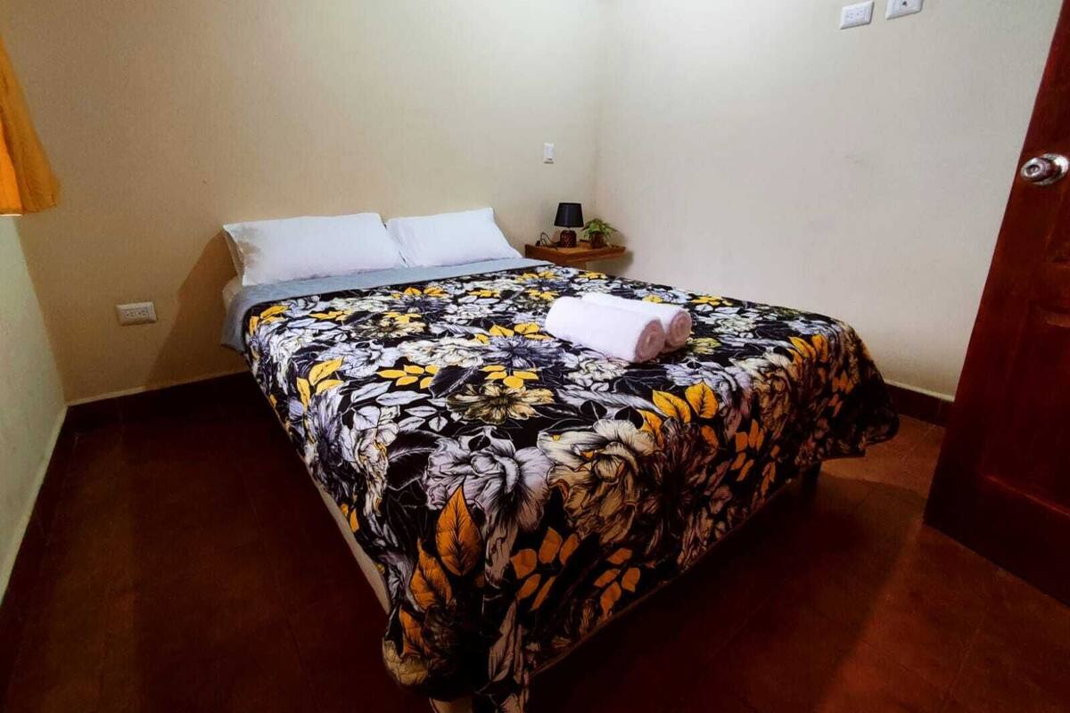 A bed with a floral bedspread, a nightstand with a lamp, and a door.