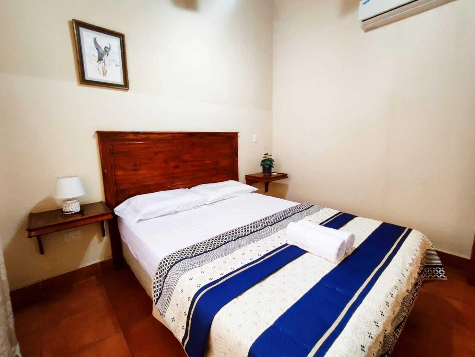 A neatly made bed with a patterned blanket, a bedside lamp, and a framed picture on the wall.