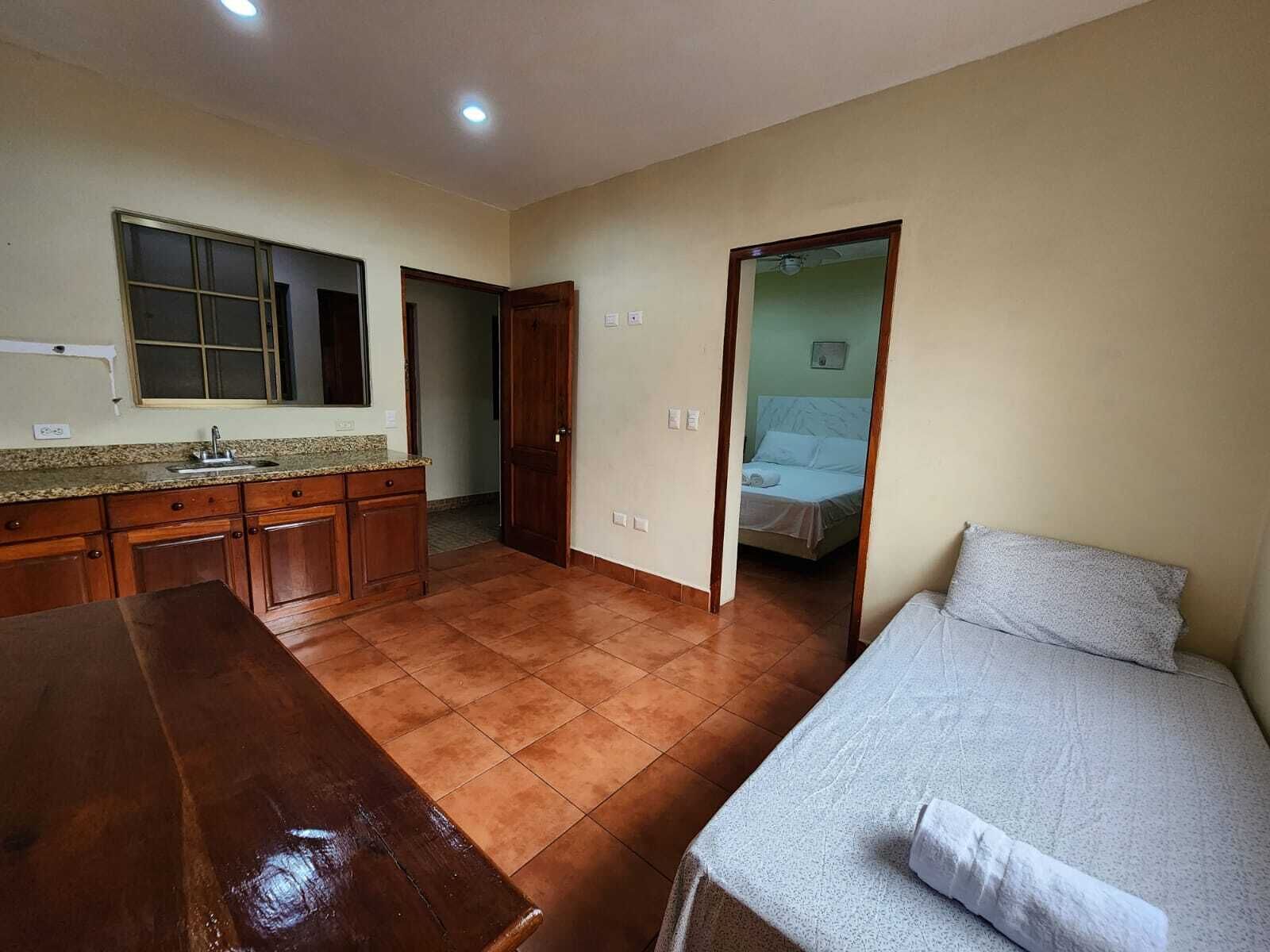 Una habitación compacta con kitchenette, una cama y una mesa de madera.