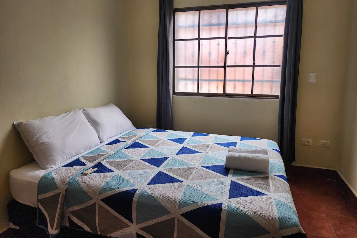 A single bed with a blue and white quilt, a white pillow, and a white blanket.